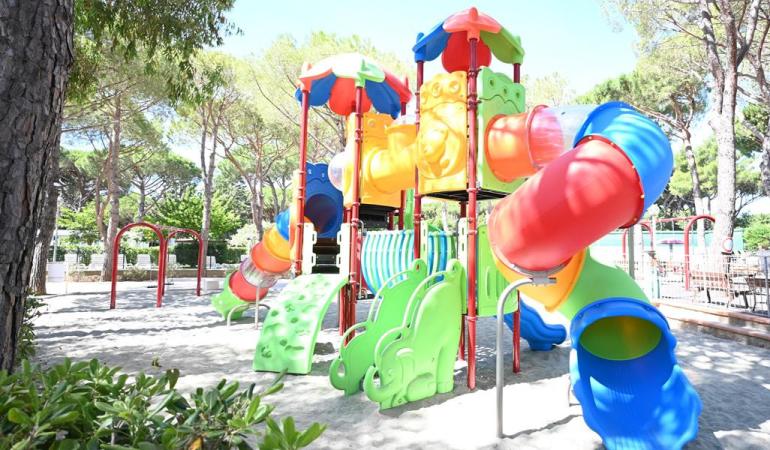 Colorato parco giochi all'aperto, scivoli e arrampicate tra alberi e sole.